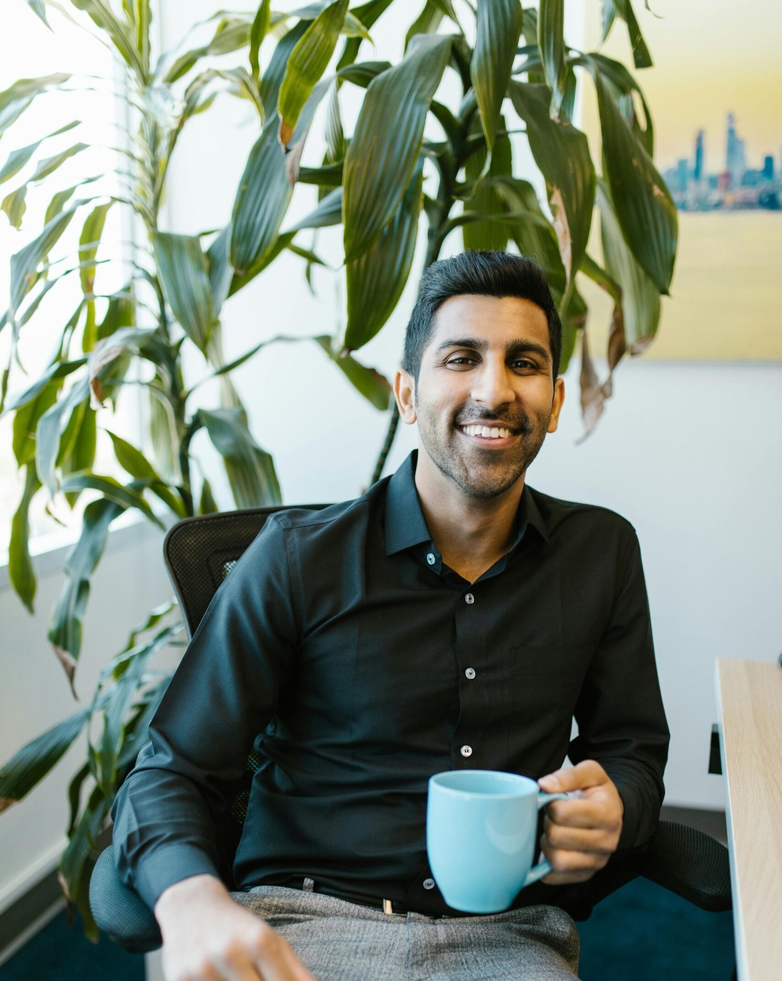 Cheerful man with coffee mug sitting in modern office with plant.
